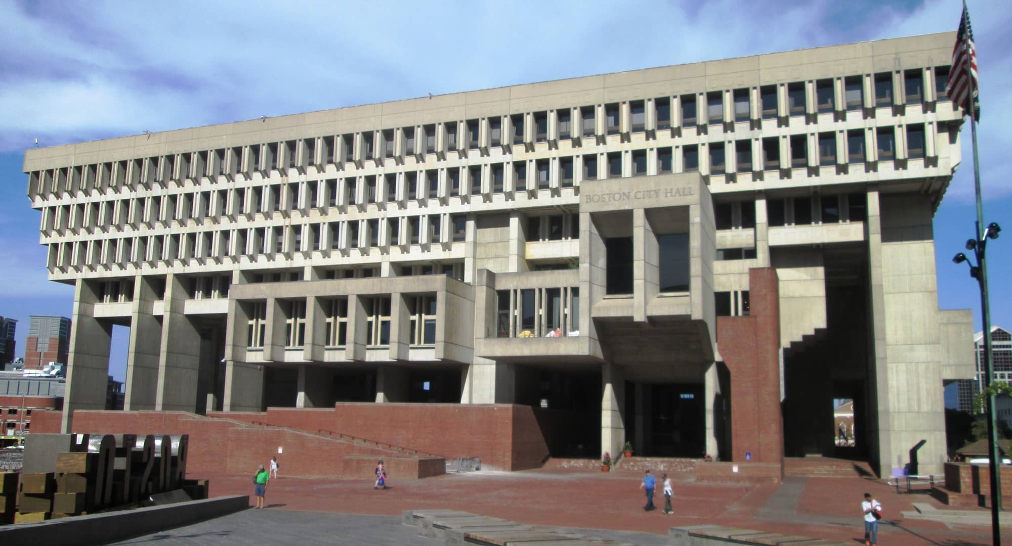 Boston City Hall, a massive brutalist concrete building with a heavy, stepped upper section over a recessed base, seen across City Hall Plaza