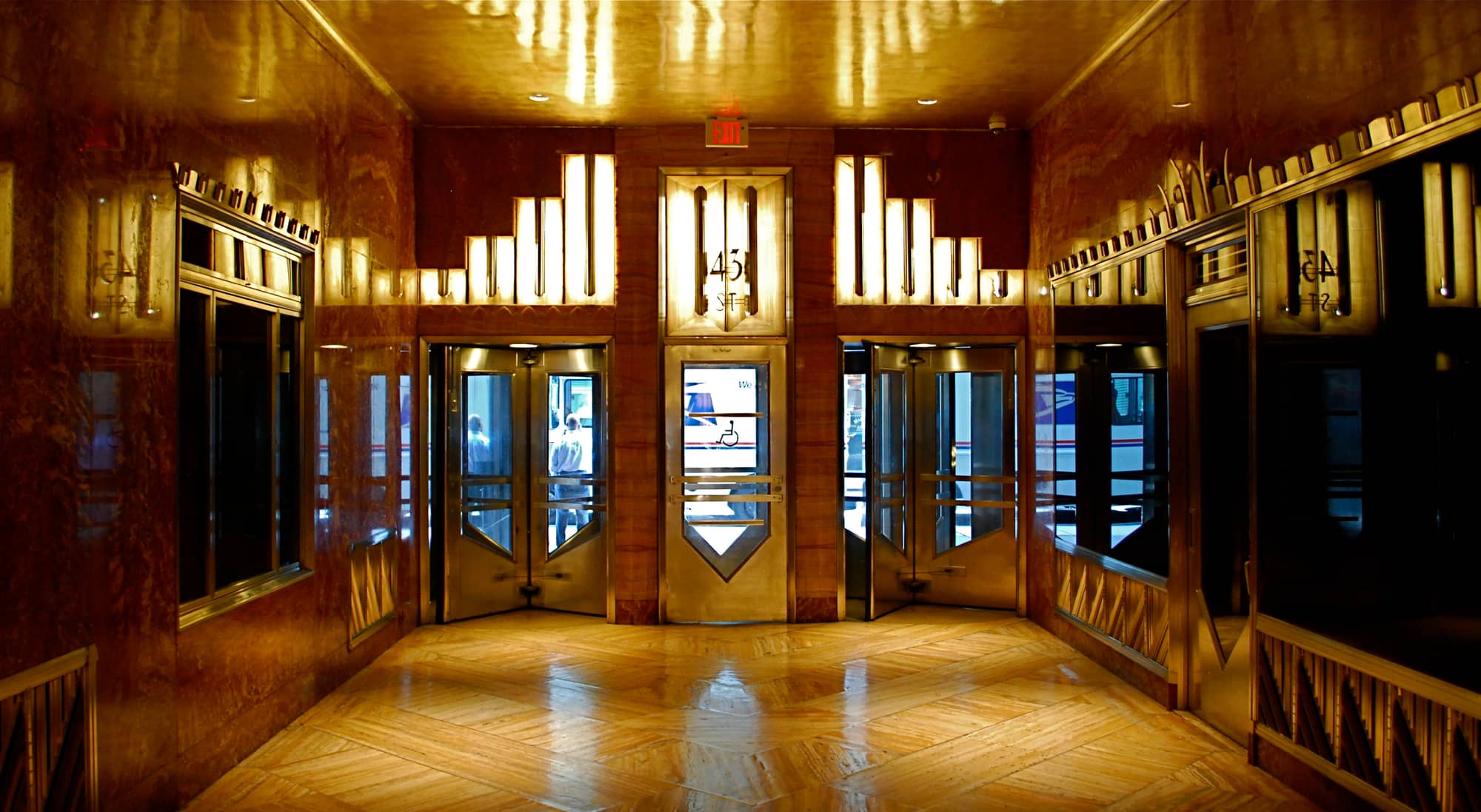The Chrysler Building's 43rd Street entrance lobby, lined in red marble with stepped, backlit Art Deco panels above chevron-shaped steel doors
