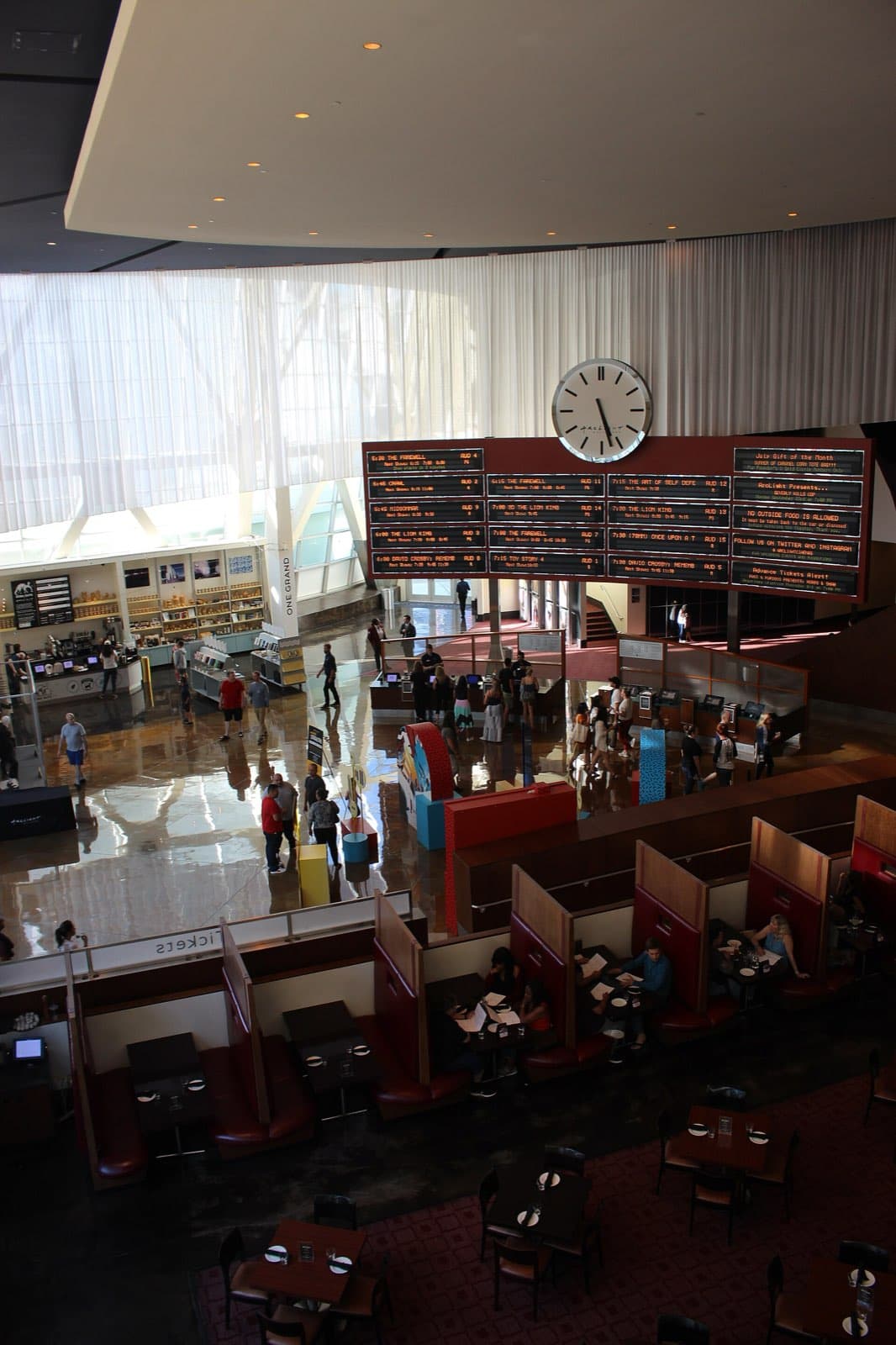 The lobby of the Cinerama Dome complex seen from the upper floor in July 2019, with a large clock, a concession counter and people moving through