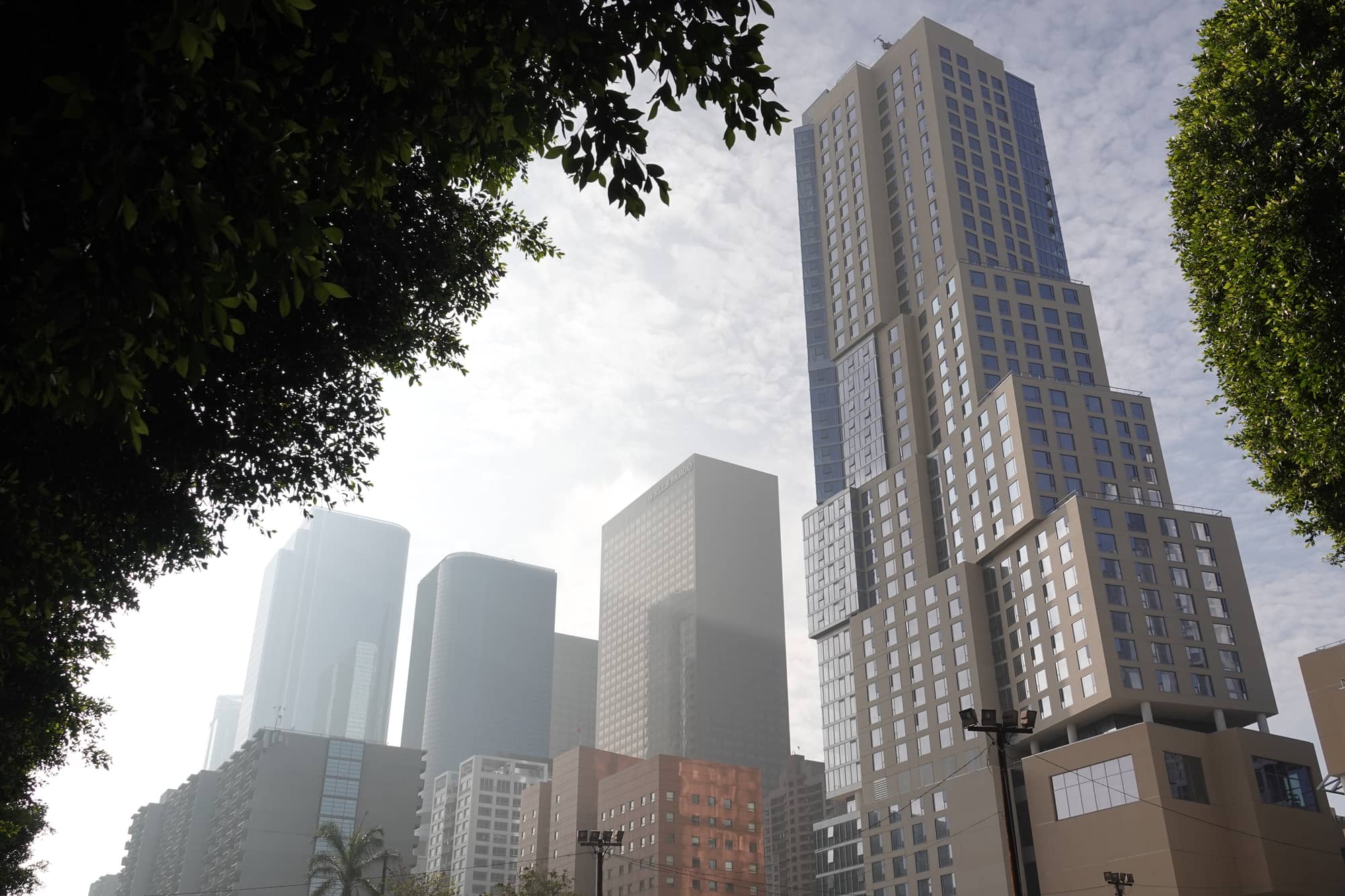 The stepped tower of The Grand, Frank Gehry's mixed-use development on Grand Avenue in downtown Los Angeles, framed by trees against hazy high-rises