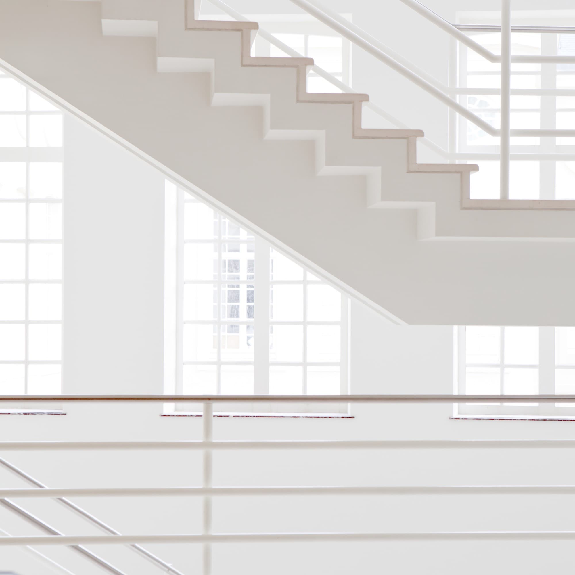 A white stair rising past tall white-framed windows inside the 1992 wing of Design Museum Gent
