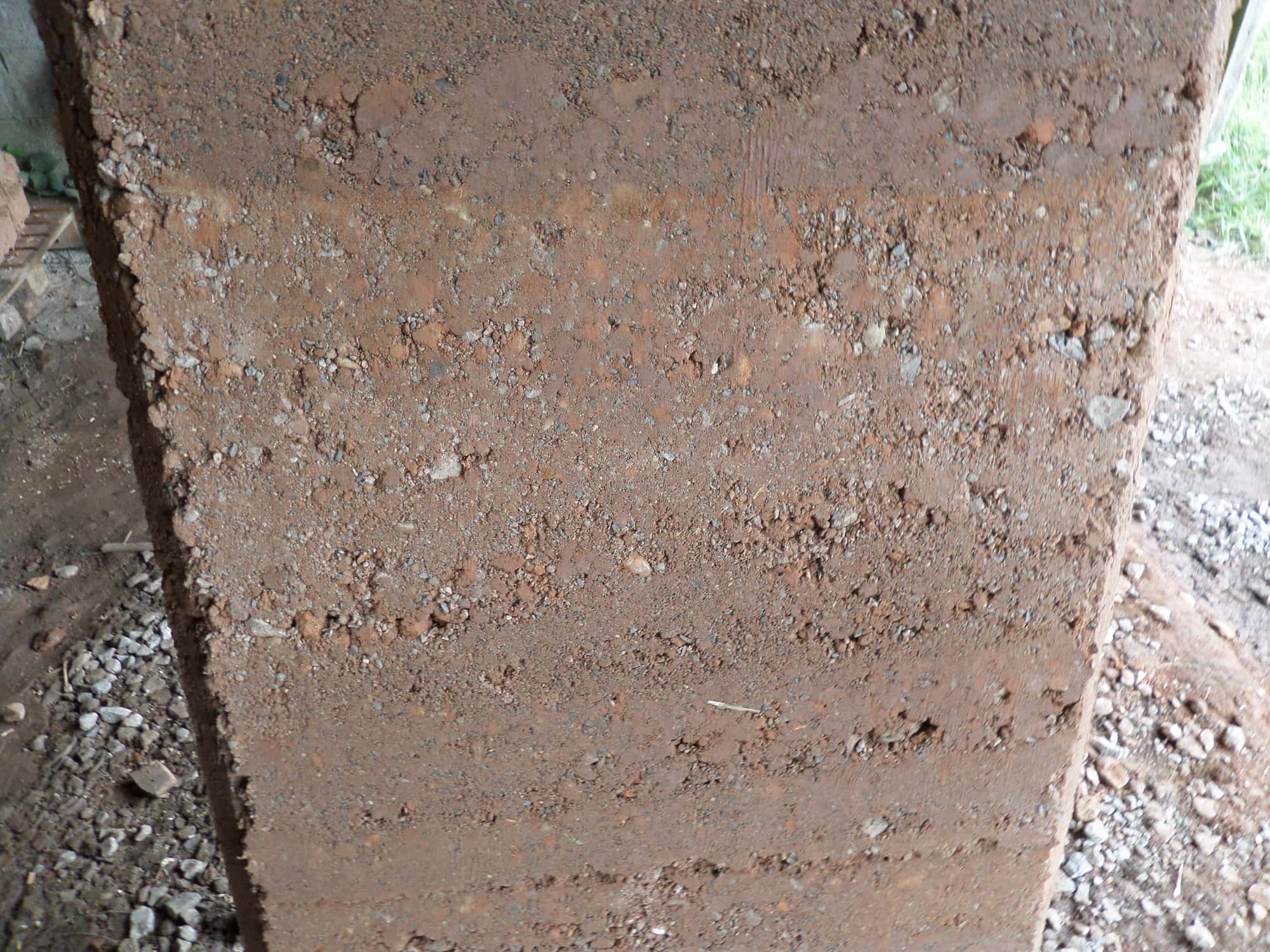 Close-up of a rammed earth wall in Cumbria, England, showing reddish compacted soil and gravel laid down in visible horizontal layers