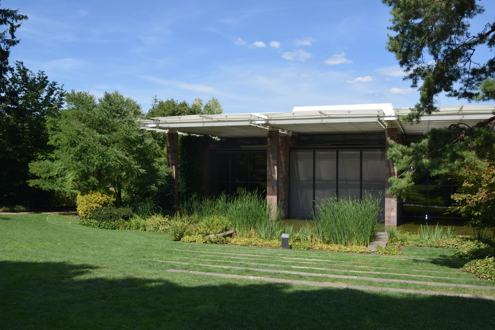 Renzo Piano's long, low glass-and-stone museum pavilion under a thin white projecting roof, seen across a sunlit lawn in Riehen