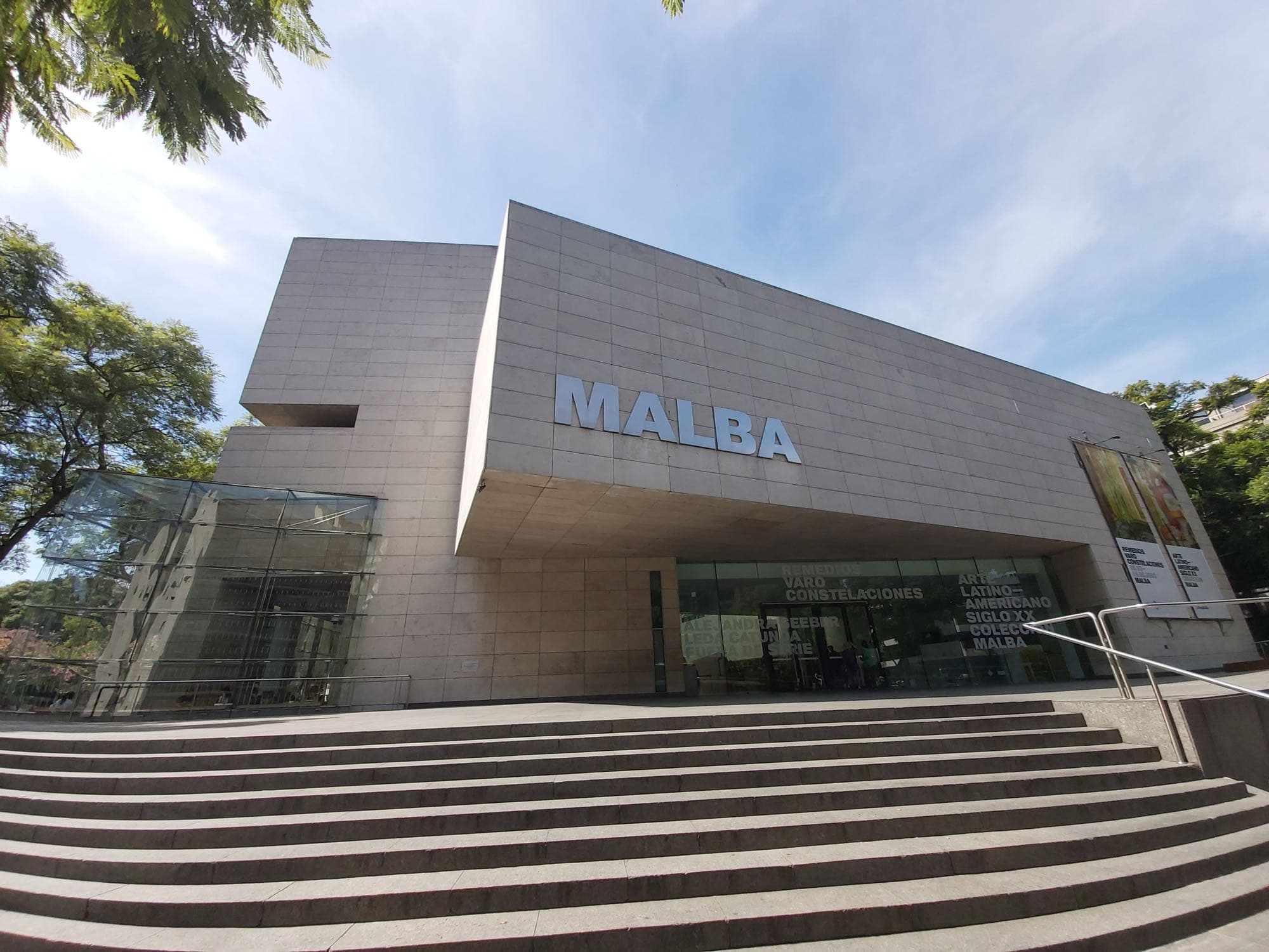 Broad stone steps rising to Malba's limestone facade in Buenos Aires, the site of the Malba expansion, with a cantilevered block lettered MALBA and a glass box at left