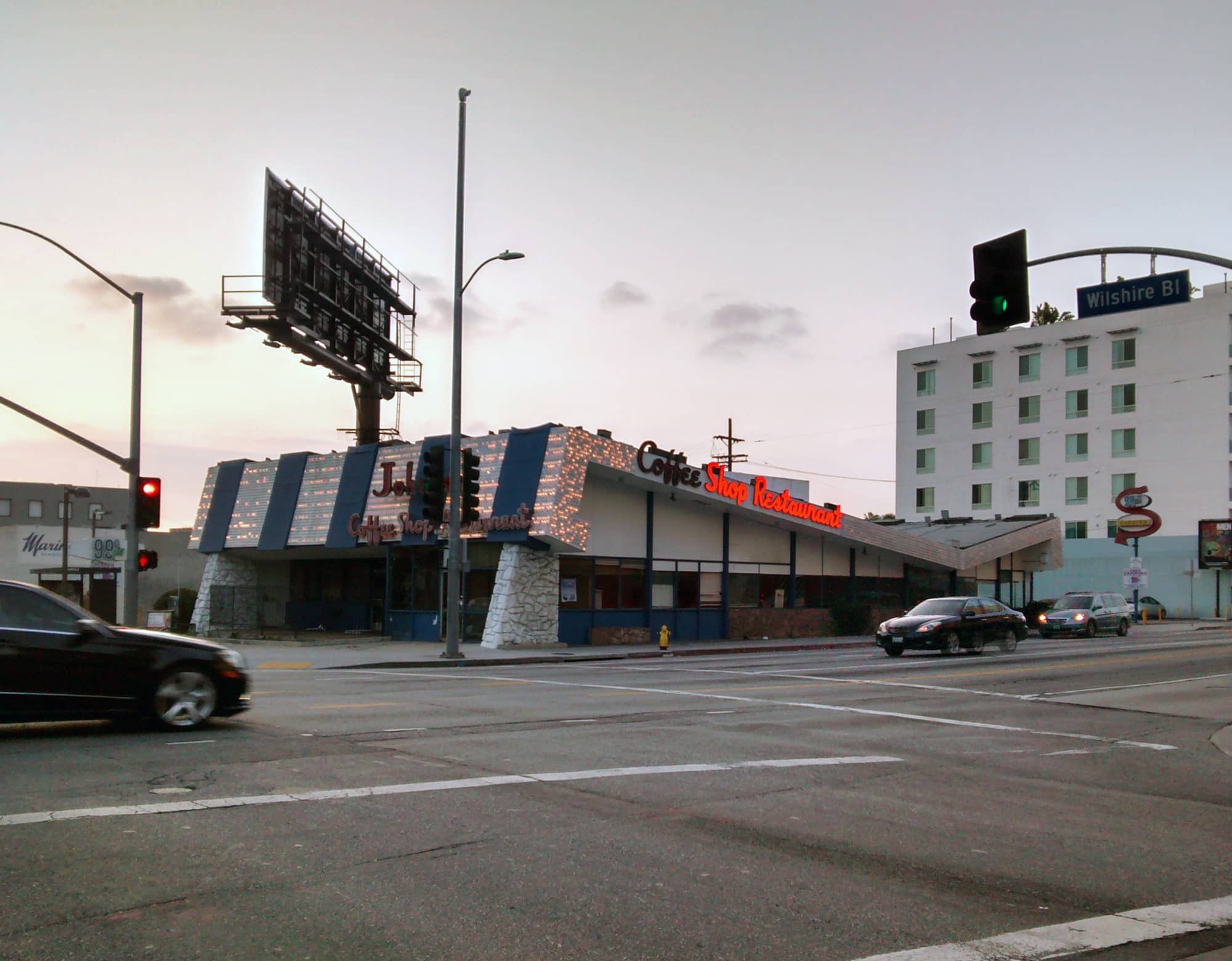 Johnie's Coffee Shop at Wilshire Boulevard and Fairfax Avenue in Los Angeles at dusk, a Googie coffee shop with a folded, striped roof and stone piers