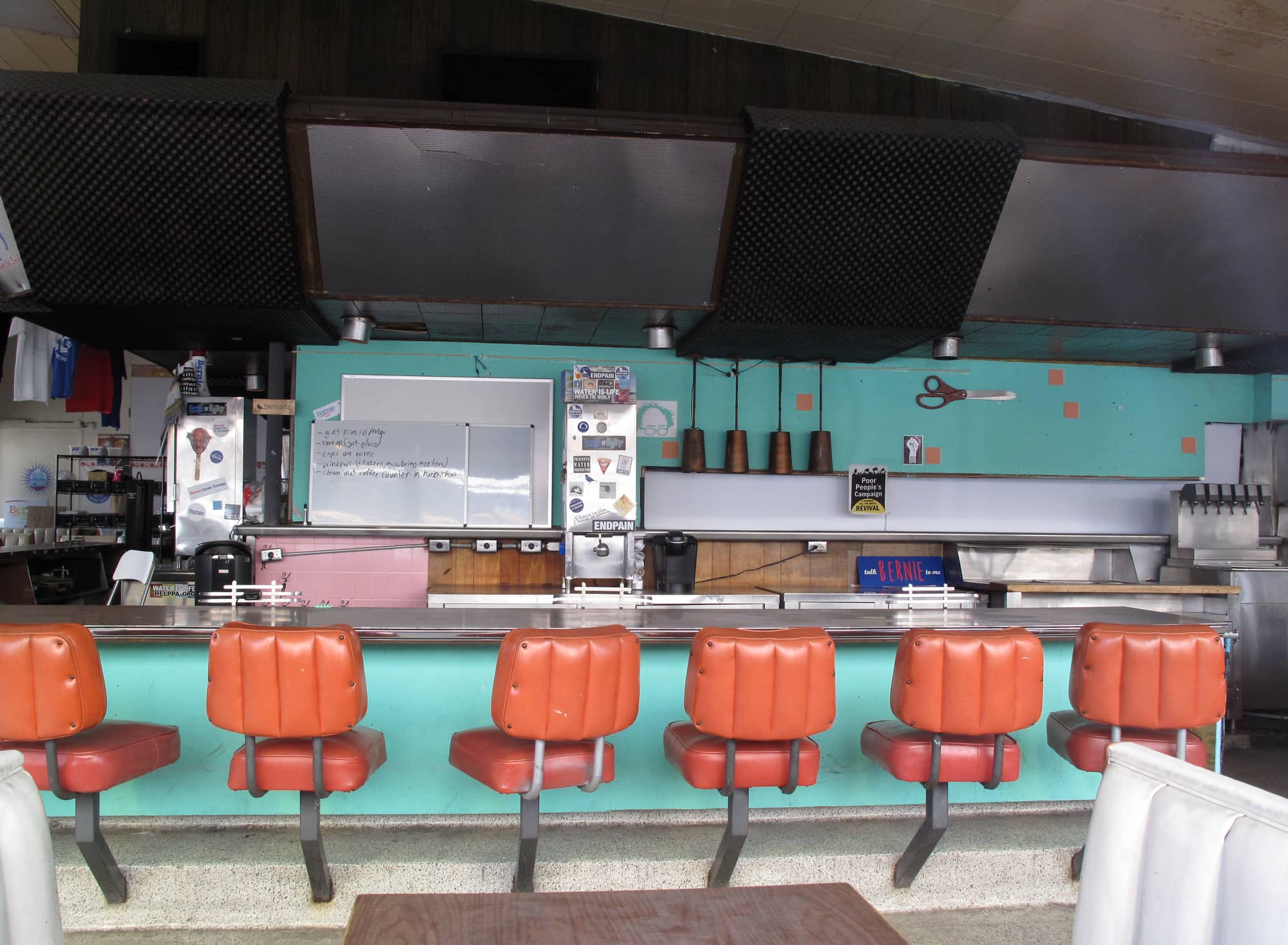 Inside Johnie's Coffee Shop in 2021: a long counter with orange swivel stools under a dark angled ceiling