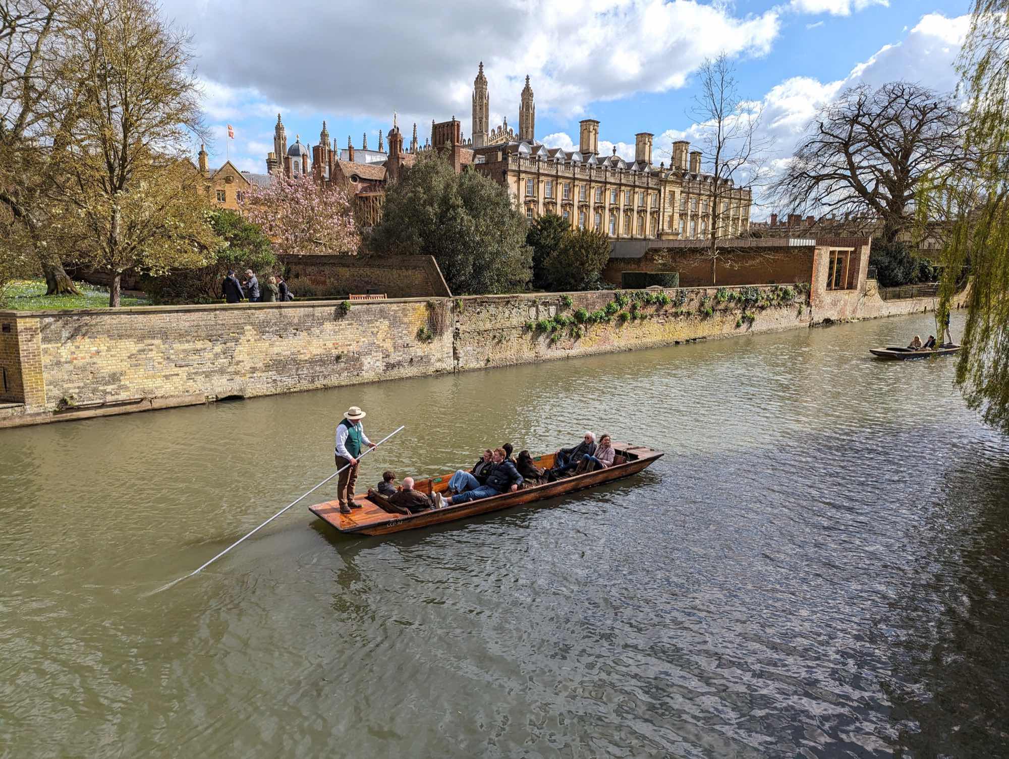 A punt on the River Cam below an ivy-hung river wall, with Clare College's classical stone ranges behind and a low flat-roofed addition facing the river at right