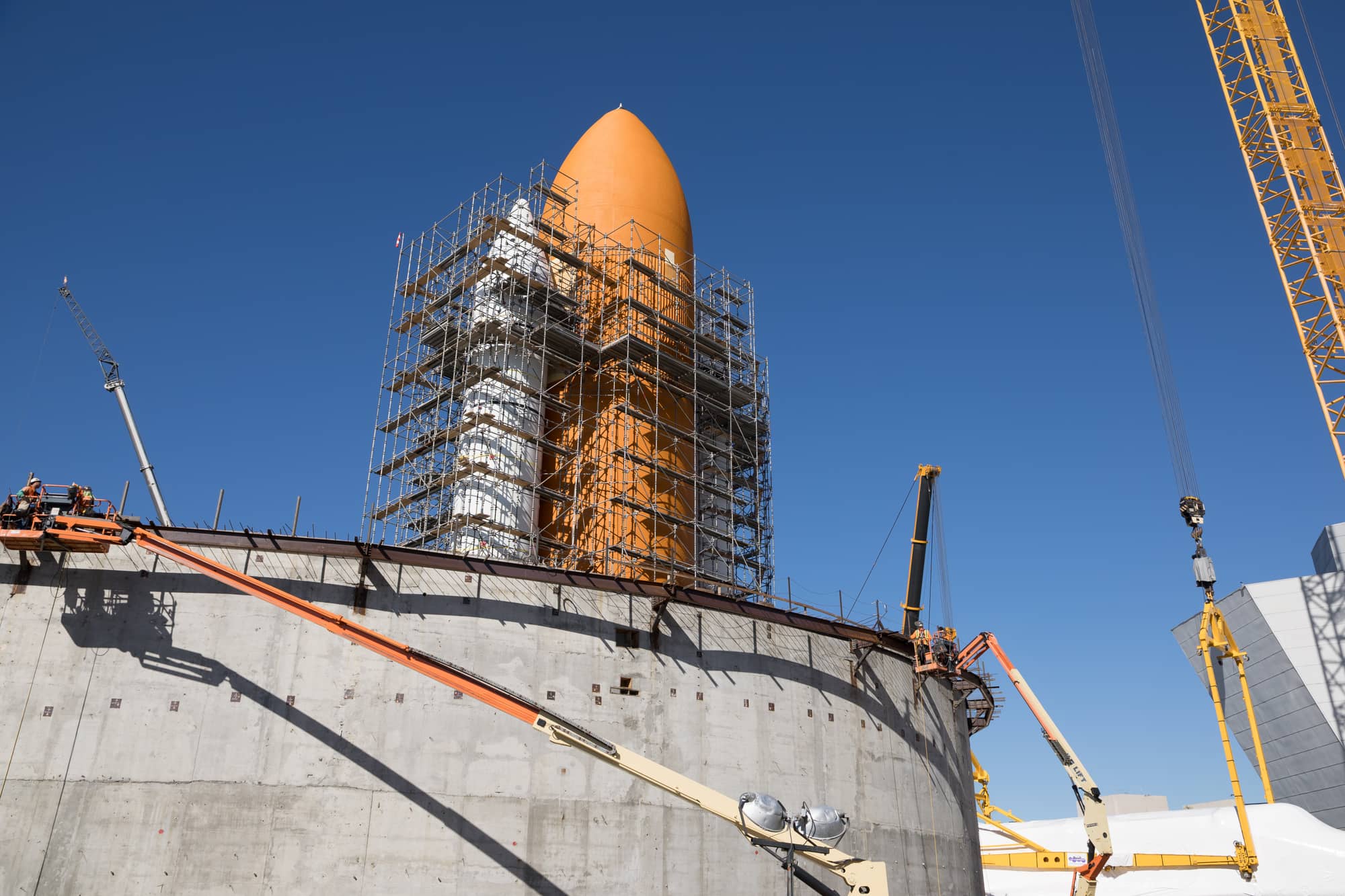 A curved concrete wall rising around Endeavour's orange external tank and white solid rocket boosters, wrapped in scaffolding, at the Samuel Oschin Air and Space Center in January 2024