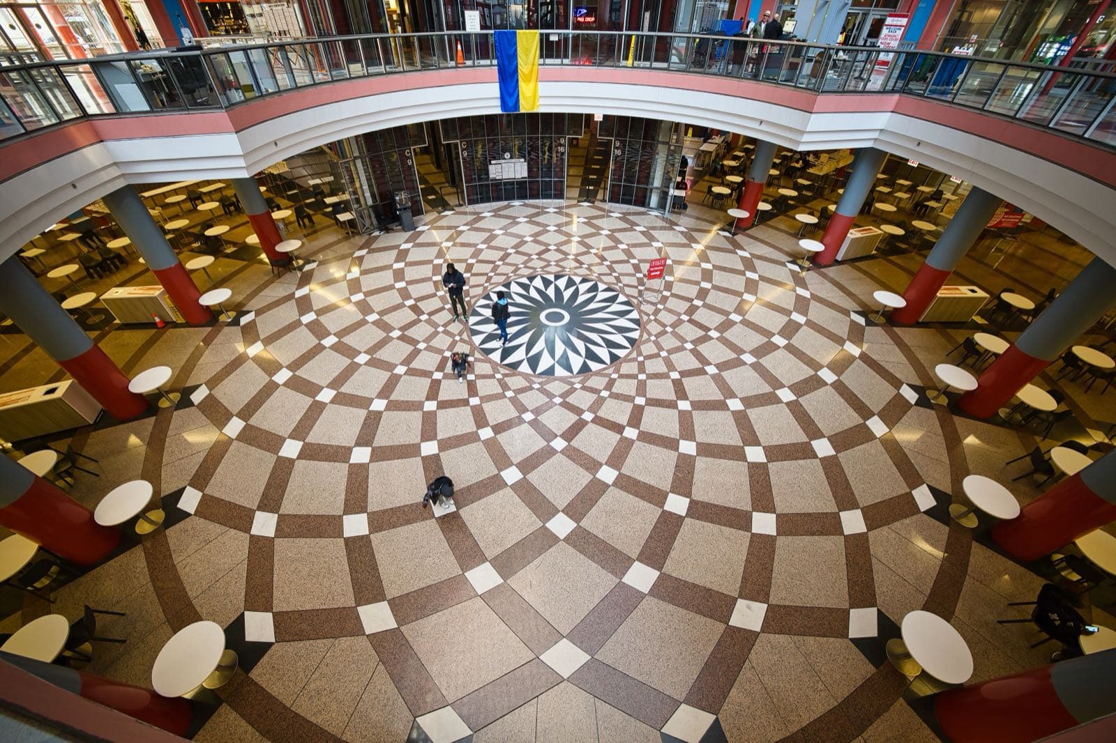 Overhead view of the Thompson Center atrium floor: a black-and-white star rosette set in radiating bands of brown and cream stone, ringed by café tables