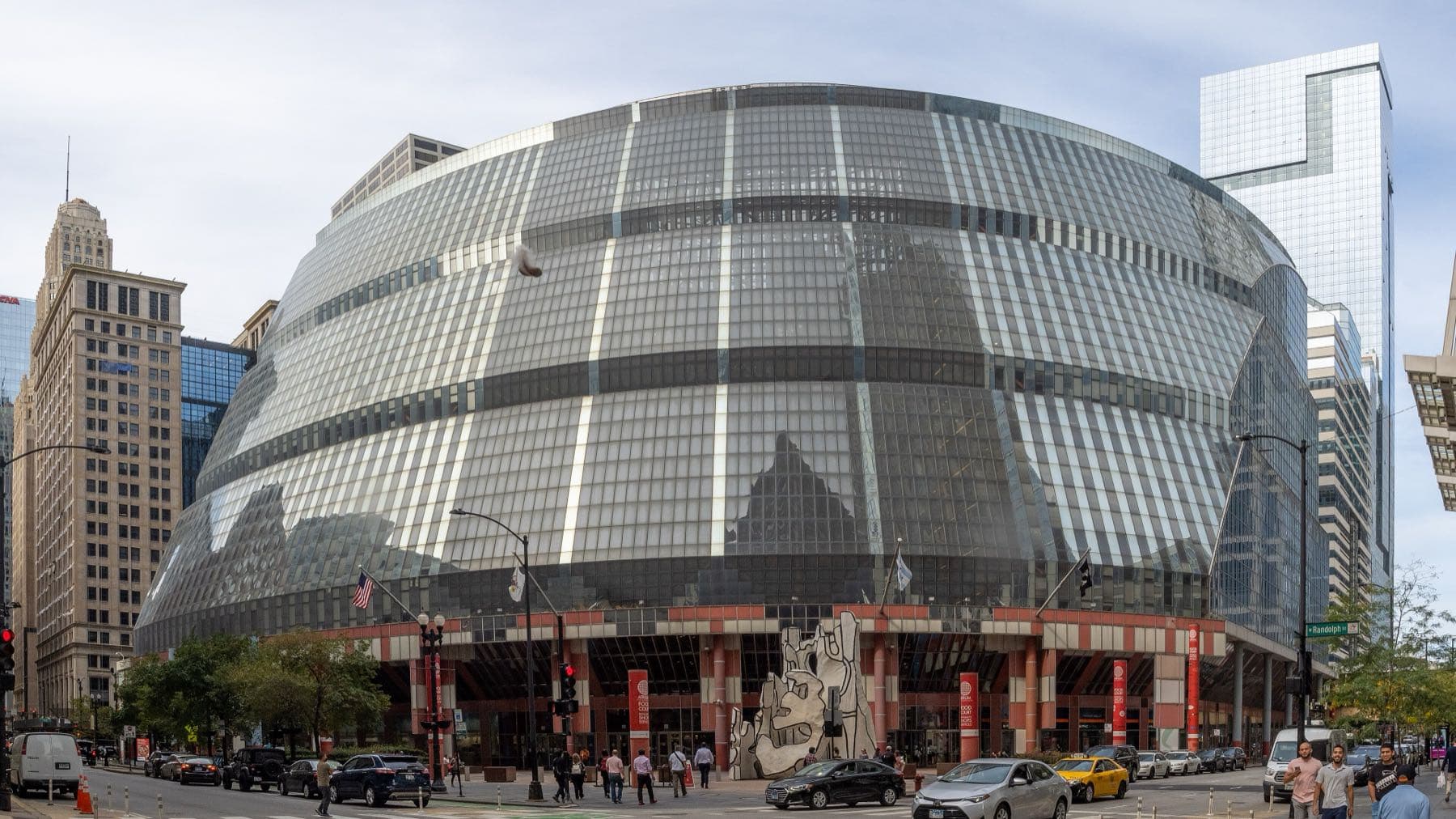 The Thompson Center in Chicago in 2021, before the Thompson Center redesign: a curved, banded glass facade sloping back above a salmon-and-grey colonnade, with Dubuffet's sculpture on the plaza
