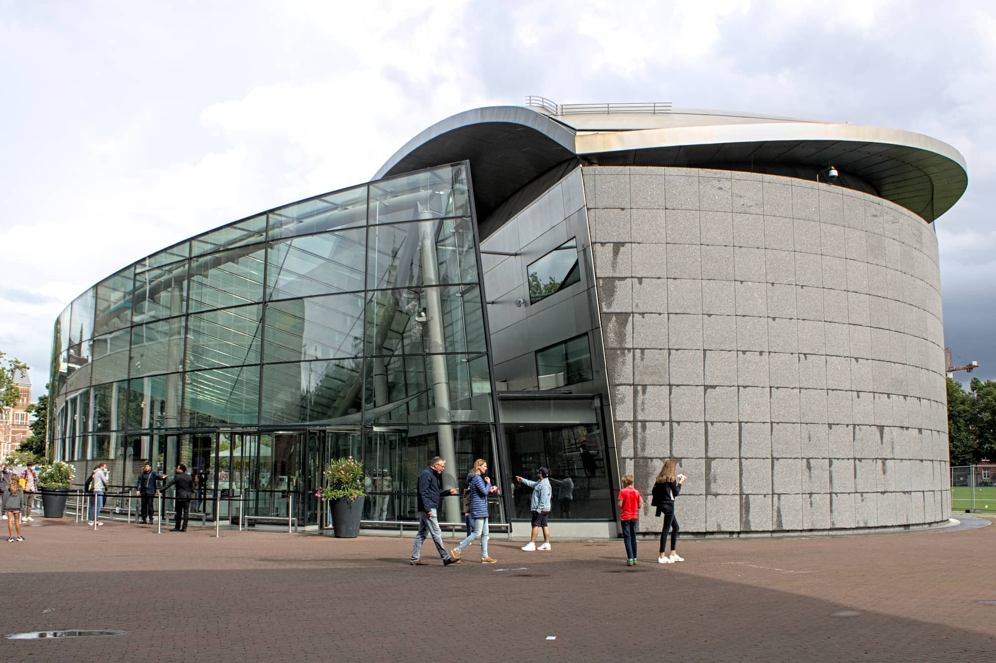 Kisho Kurokawa's elliptical, stone-clad Exhibition Wing of the Van Gogh Museum with the curved glass entrance hall of 2015 and visitors on the square in front