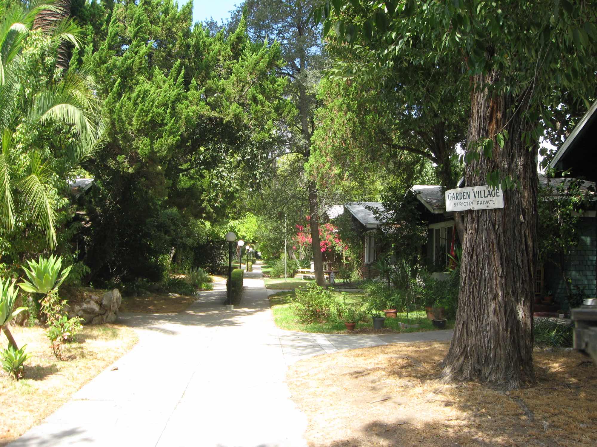 Shaded walkway with lamp posts past dark-shingled Craftsman bungalows at Bowen Court; a sign reads Garden Village, Strictly Private