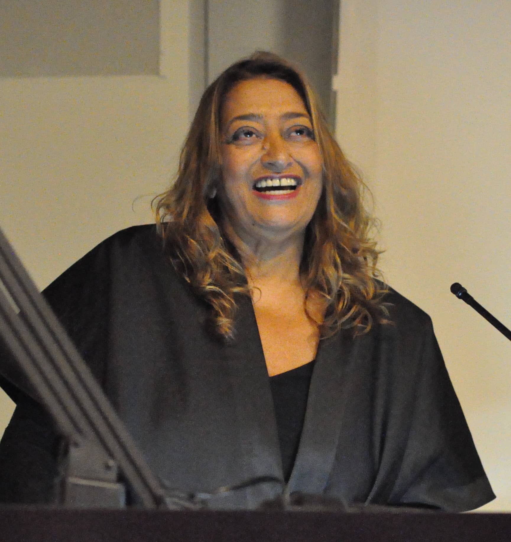 Zaha Hadid smiling at a lectern during a talk at Columbia University in November 2011
