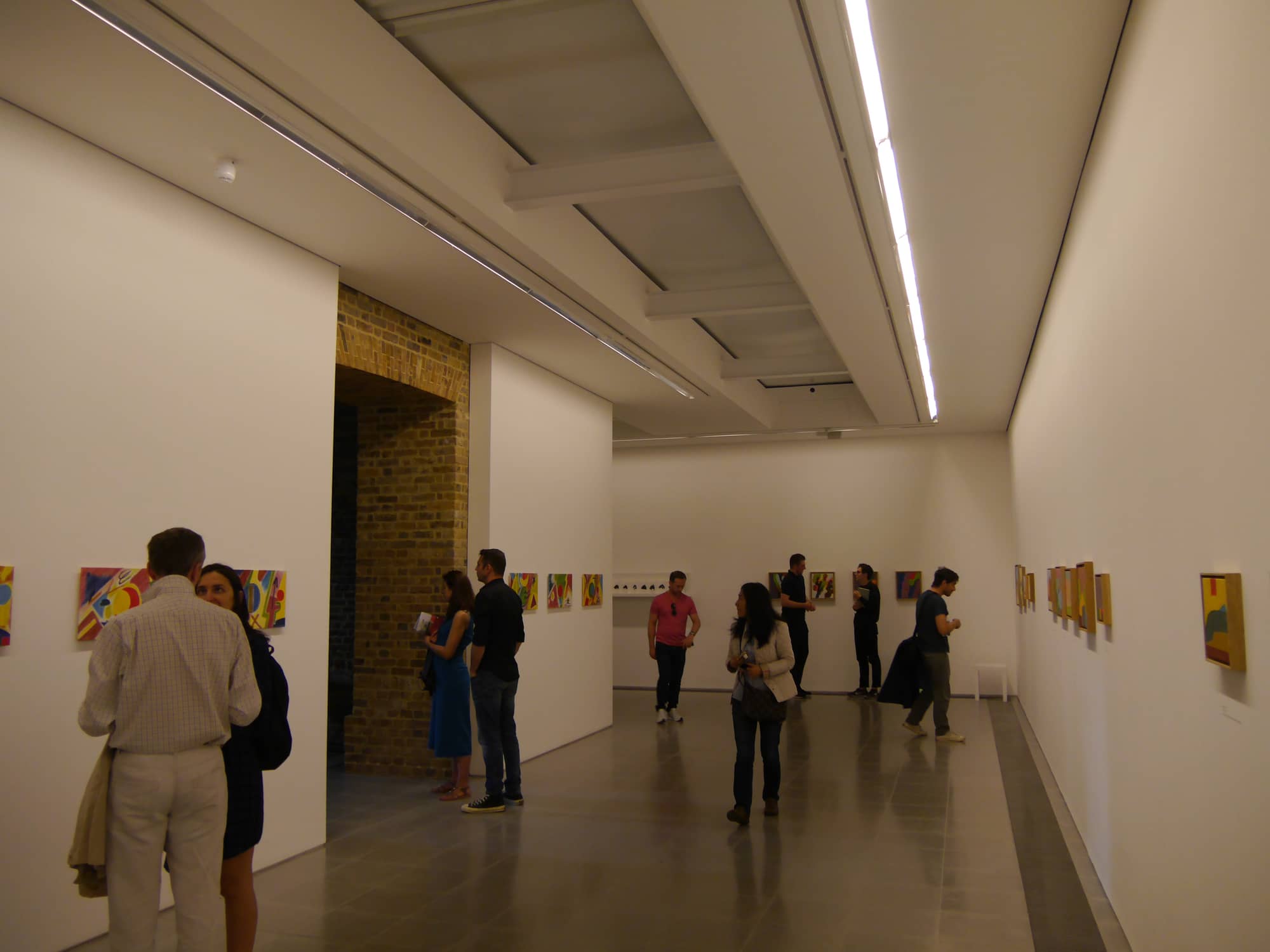 Visitors in a white-walled gallery of the Serpentine Sackler Gallery in Kensington Gardens, with an exposed brick arch on the left